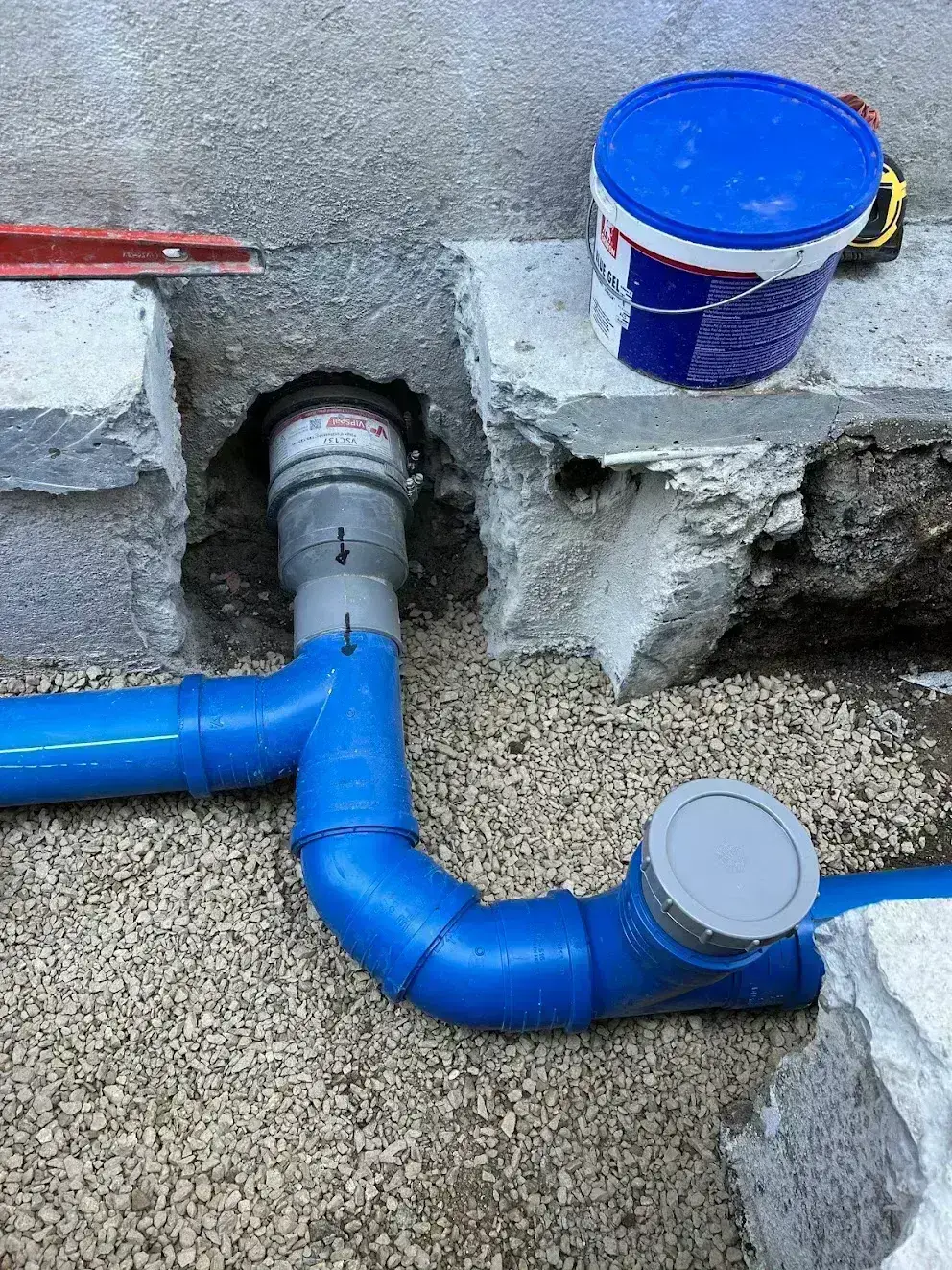 Pose et scellement d'un raccord PVC bleu dans la fondation, mise aux normes d'assainissement en Finistère Sud