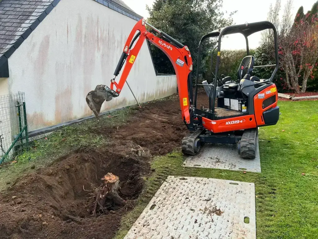 Extraction d'une souche le long du pignon d'une maison à la mini-pelle, dessouchage en Finistère Sud