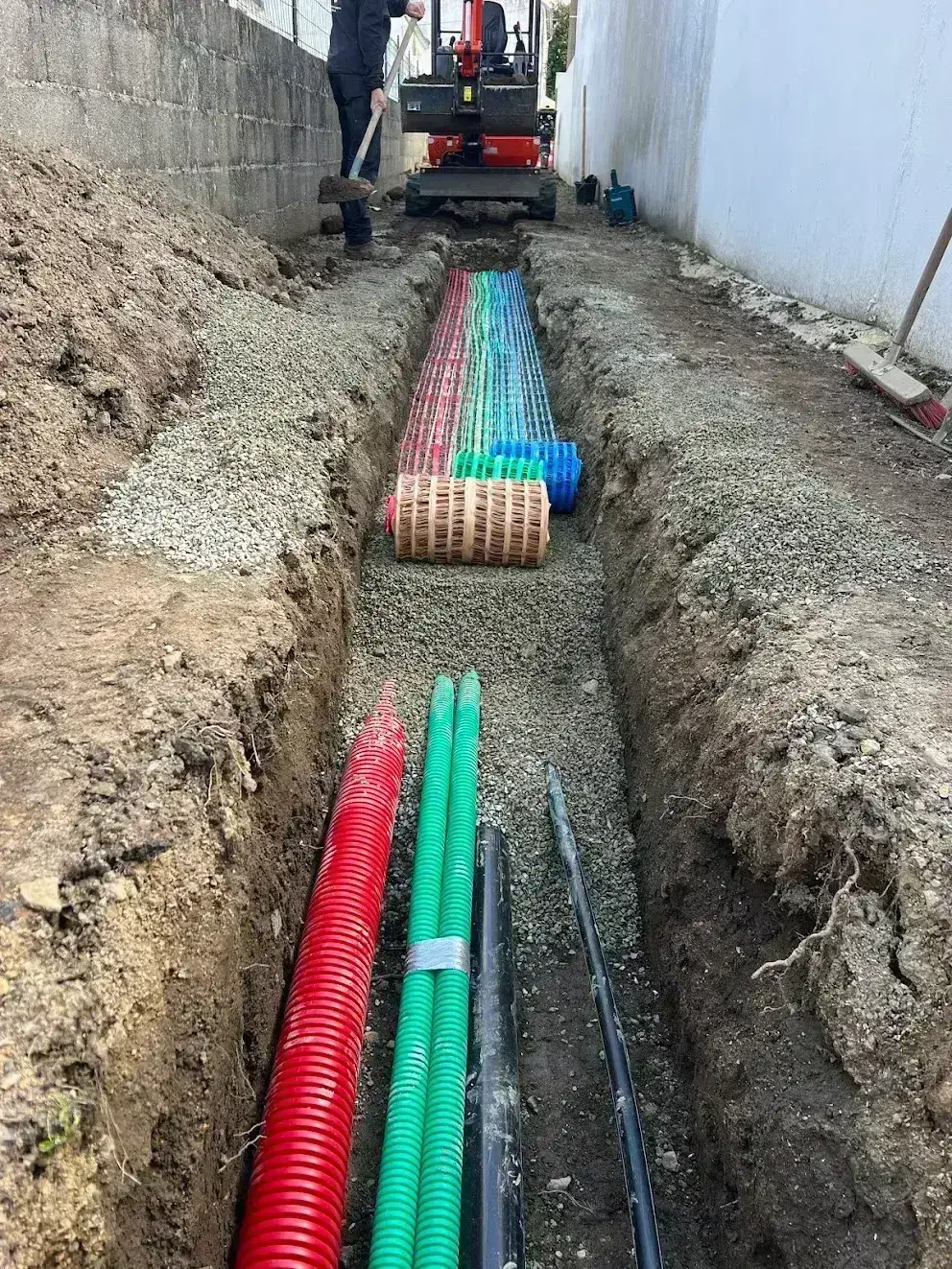 Tranchée technique étroite entre deux murs, pose de gaines TPC et grillage avertisseur à la mini-pelle Kubota, terrassement en Finistère Sud
