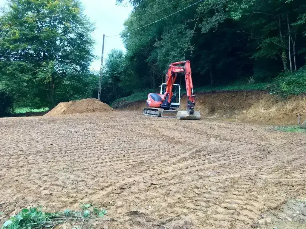 Talus décaissé et terrain nivelé en lisière de bois à la pelle Kubota rouge, terrassement en Finistère Sud