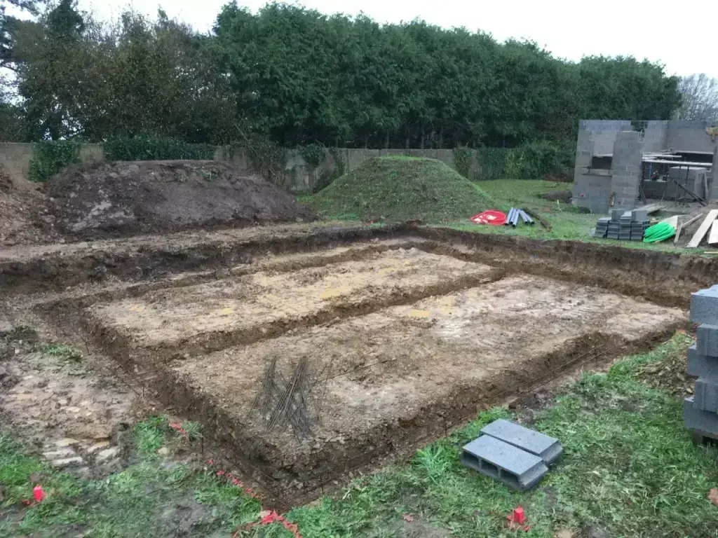 Fouilles de fondations avec armatures en attente et parpaings le long d'une haie de cyprès, terrassement en Finistère Sud